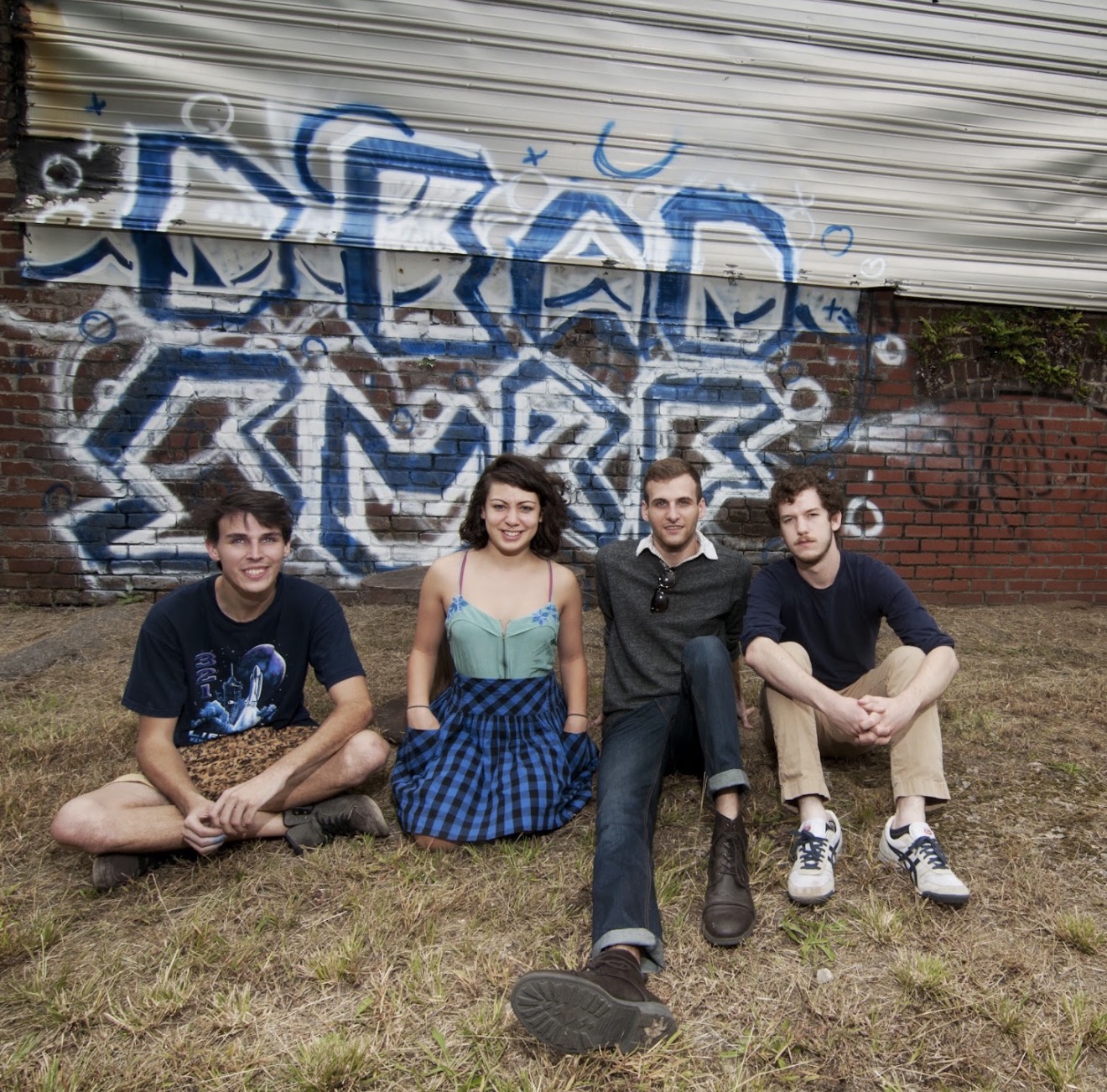 The four members of Dead Surf seated together in front of a painted brick wall